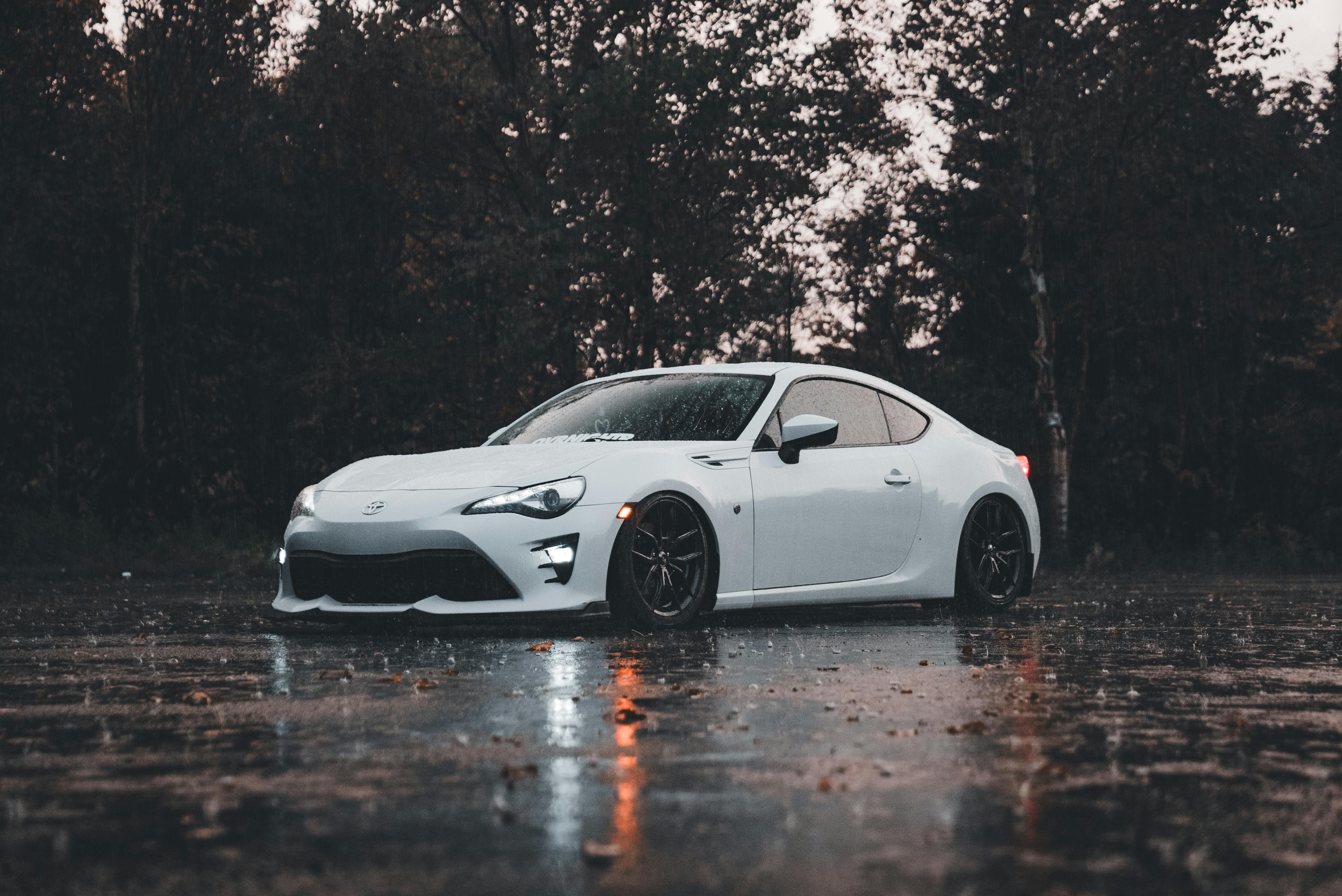 White sports car parked on a wet road with trees in the background